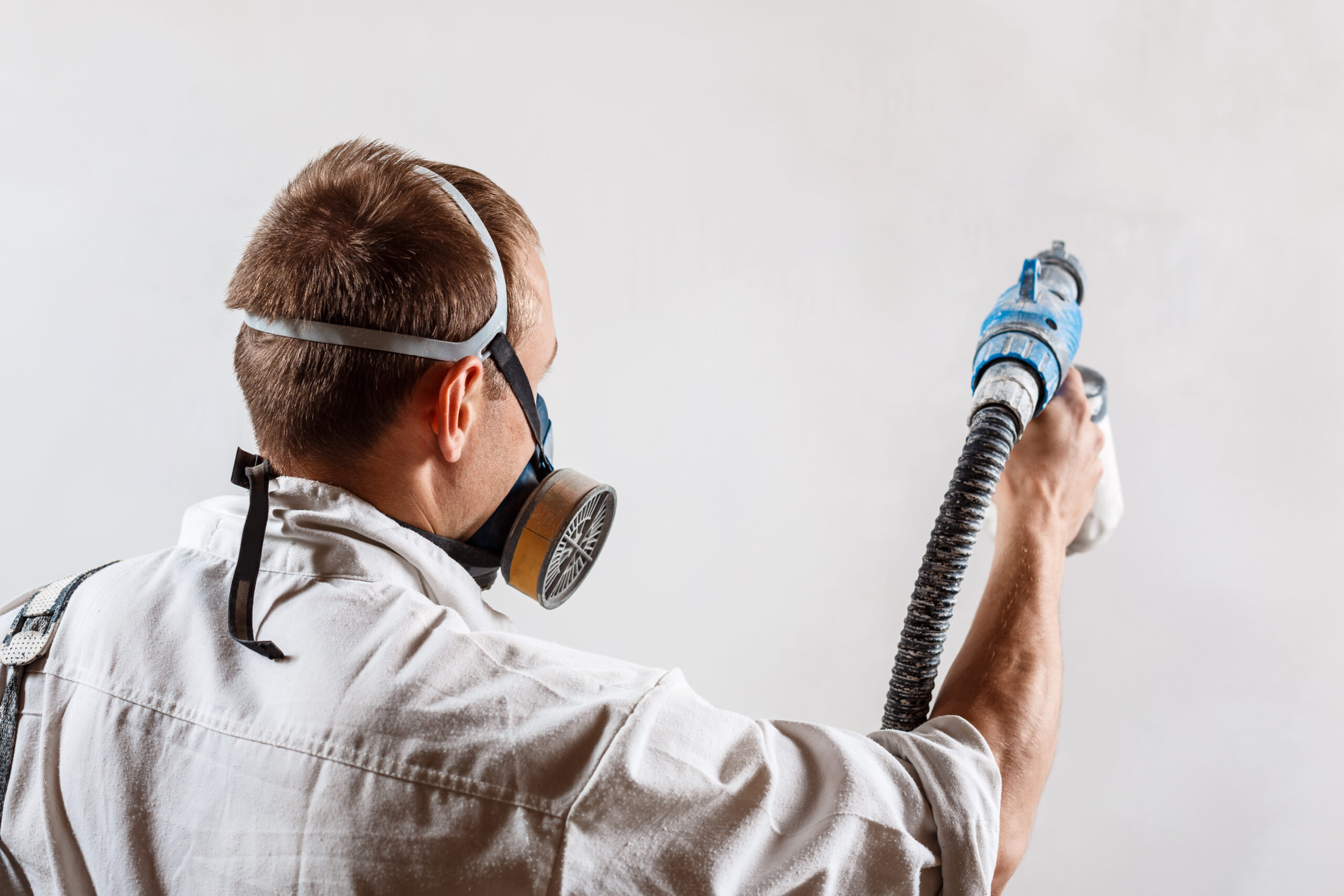 Worker painting wall with spray gun in white color.